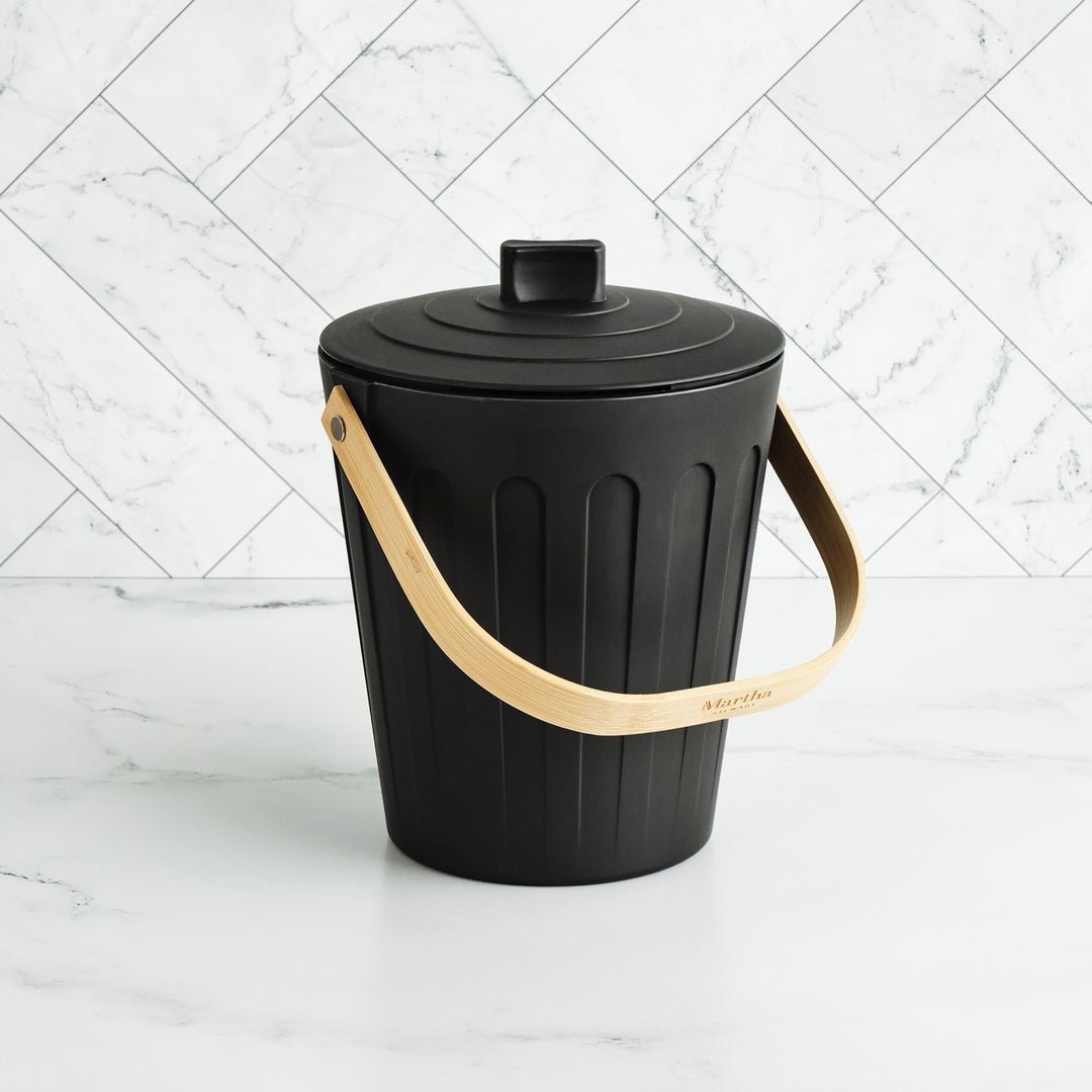 Black trash bin with a beige handle on a white marble background